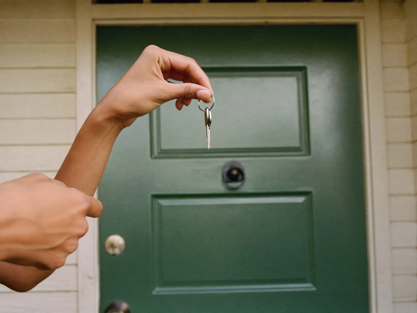 A hopeful New Zealand couple holding the keys at the front door of their first home